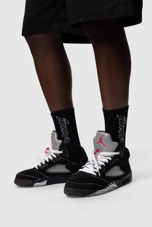 Person wearing black sneakers with red accents and black socks with white text on a white background